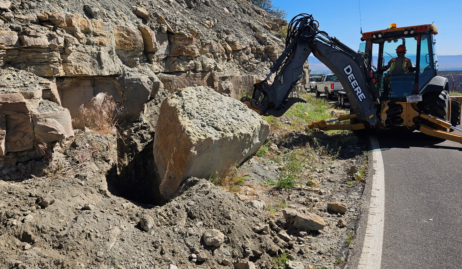 Photo of a backhoe moving rocks along the side of a road.
