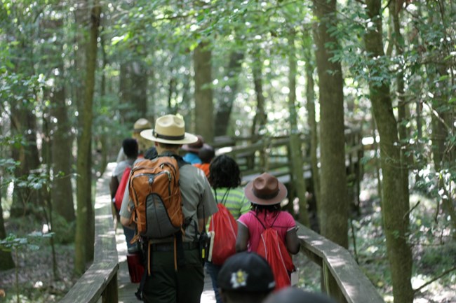Park Ranger walking with a school group on a board walk between trees.