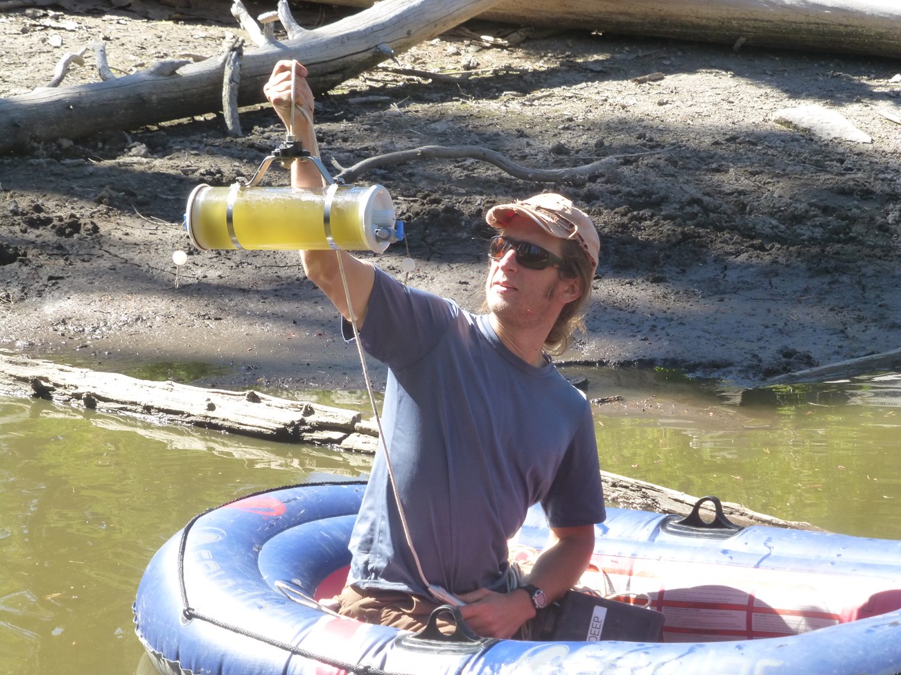Technician in a raft on a shallow lake holding up a container of murky lake water.