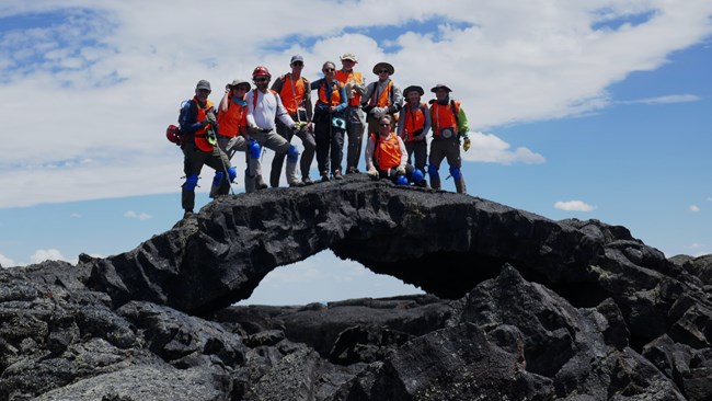 Group of people standing on an arched rock formation.