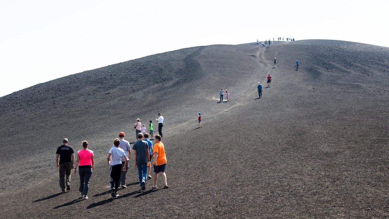 photo of groups of people walking on a barren scoria slope