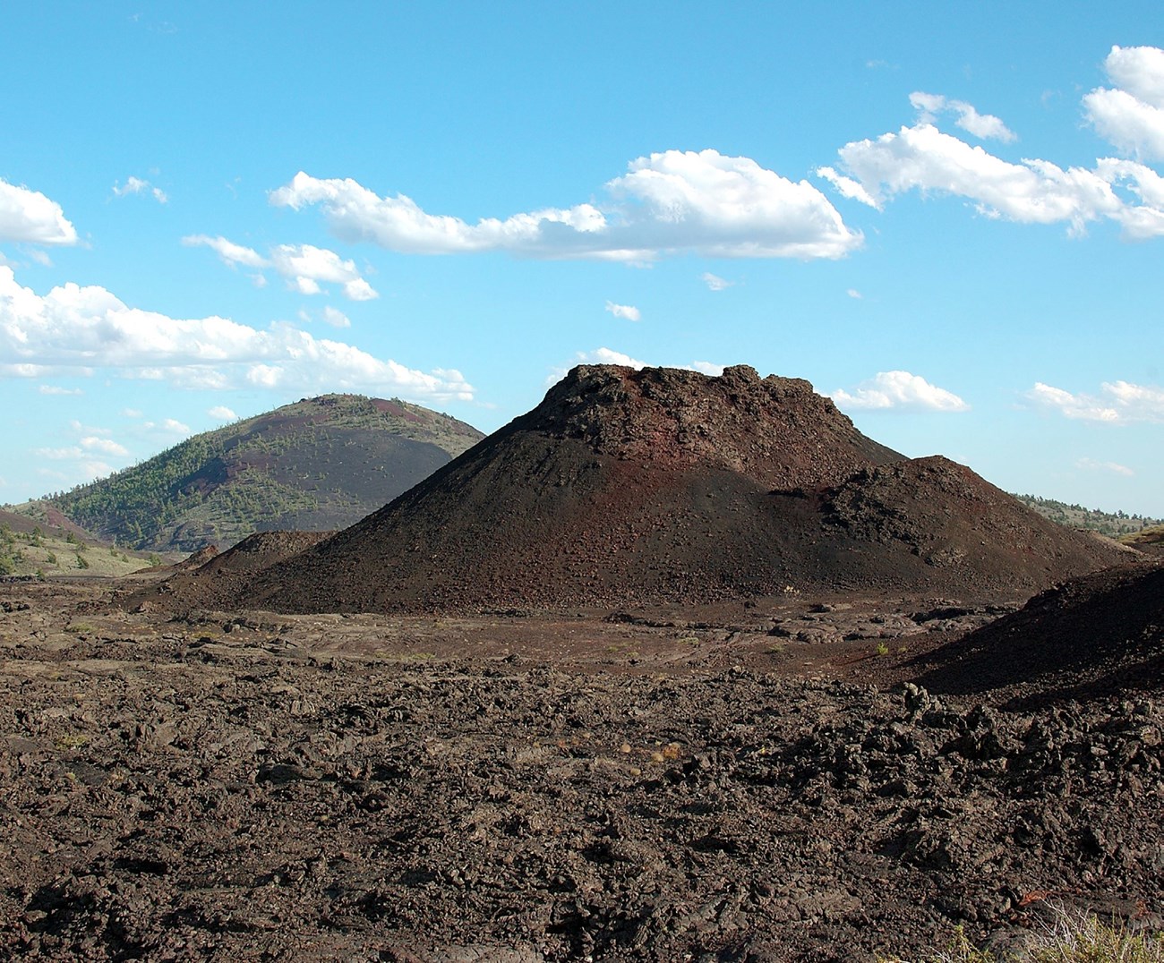 photo of a rocky volcanic cone with a large rounded volcanic peak in the distance