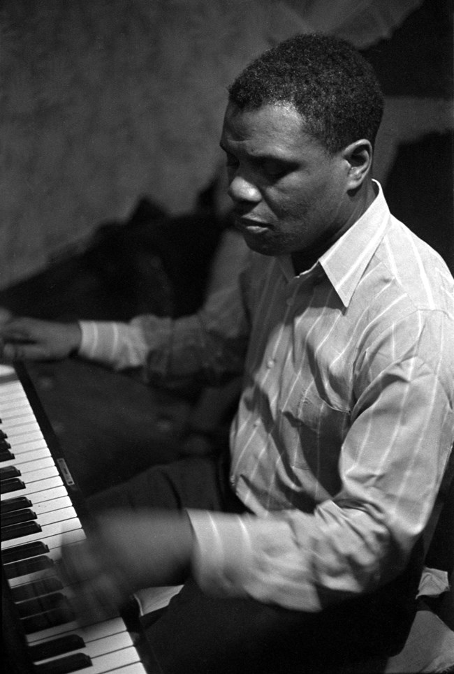 Close up of an African American man in a striped dress shirt playing piano.