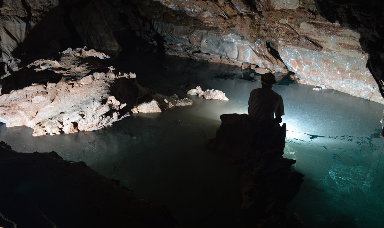 a caver silhouetted against a clear blue underground lake