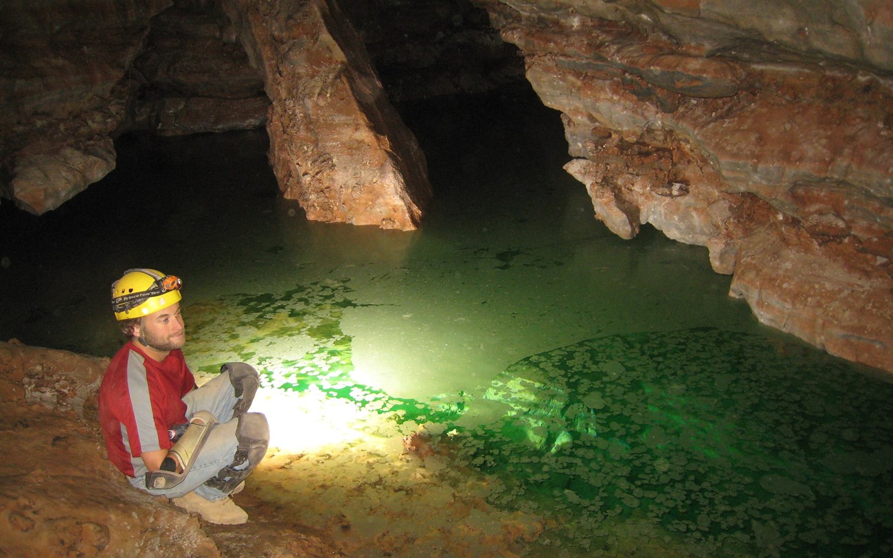 a caver sitting on the edge of an underground lake dyed green