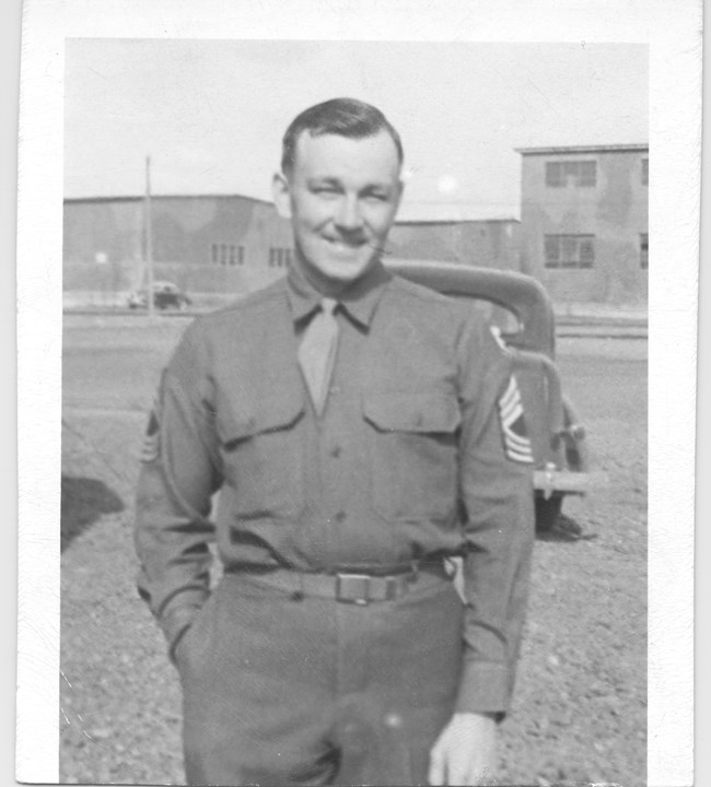 Man in uniform standing in front of an old car and building