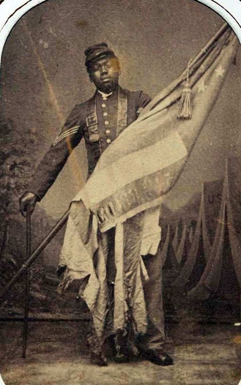 Sepia-toned historic photograph of Sgt. William Carney holding the Massachusetts 54th colors, c. 1864.