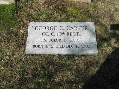 Light grey gravestone, with inscription, in the ground, surrounded by green grass, in a cemetery