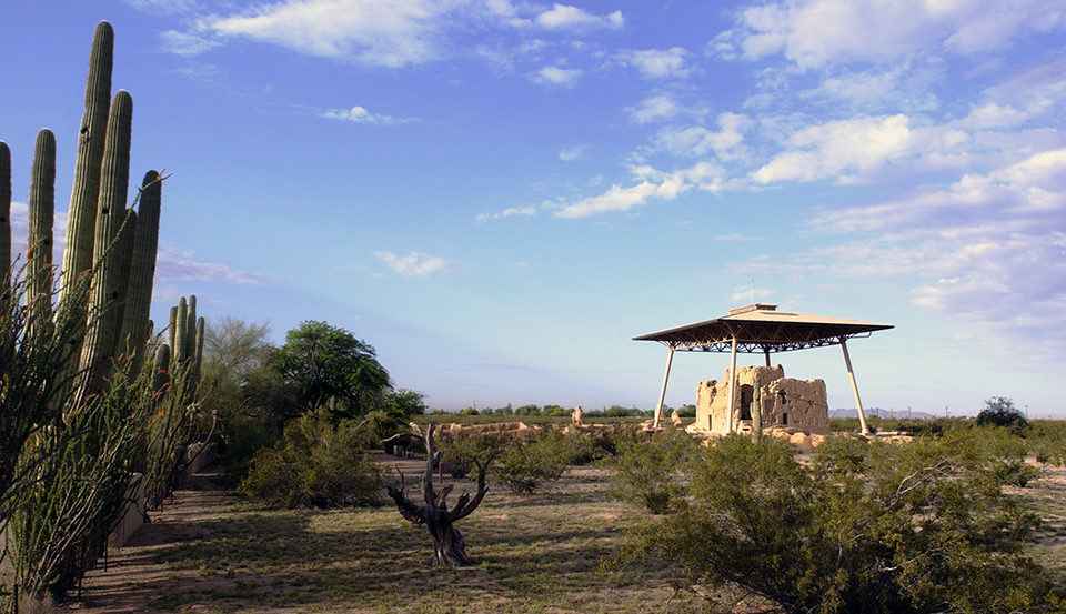 Casa Grande, a partially eroded large adobe structure, under a protective modern roof with saguaro cactuses and mesquite in the foreground.