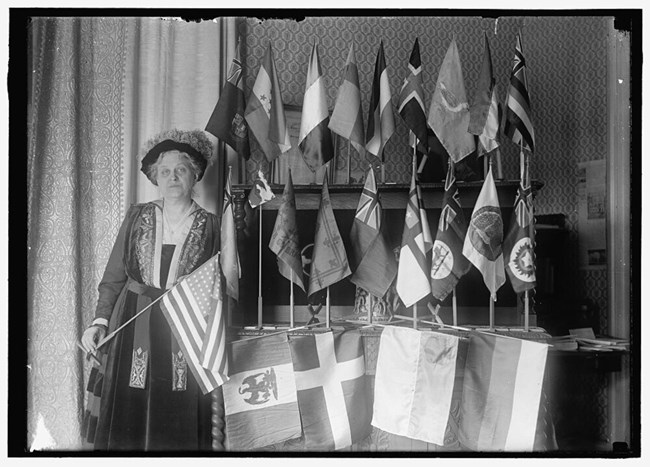 Black and white photo of Carrie Chapman Catt posing with flags from 22 nations. LOC