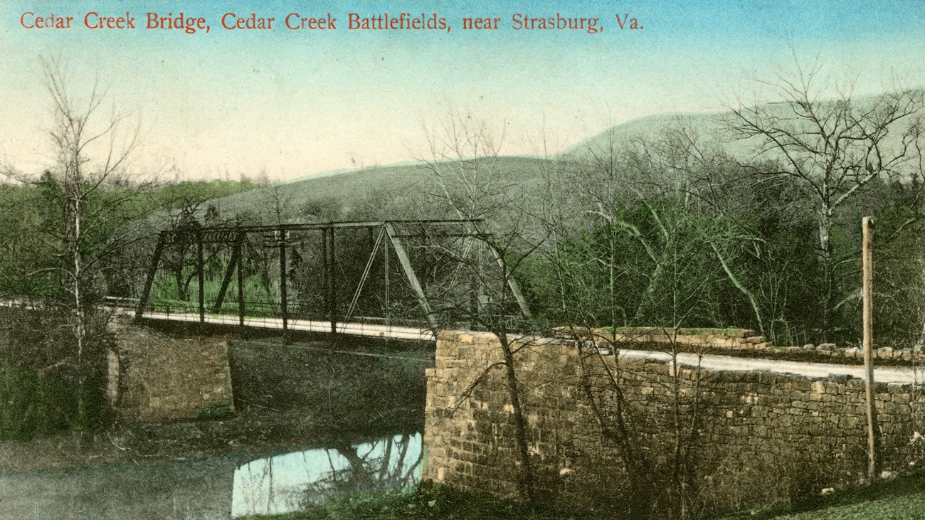 Historic postcard of a paved road on a steel truss bridge over a calm creek.
