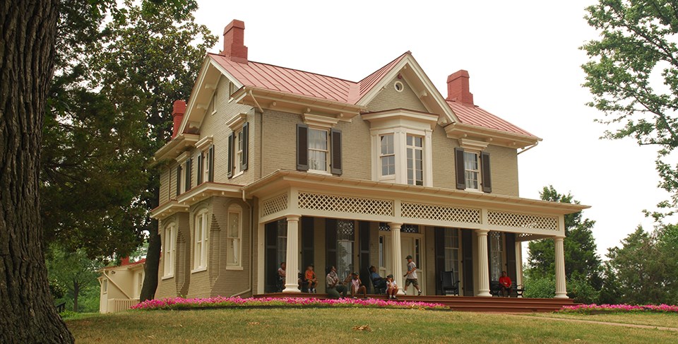 a two-story house on a grassy hill with a wraparound porch