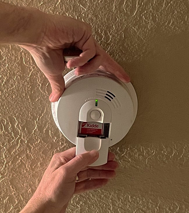 Changing smoke detector batteries A person slides the battery compartment off of a smoke detector.
