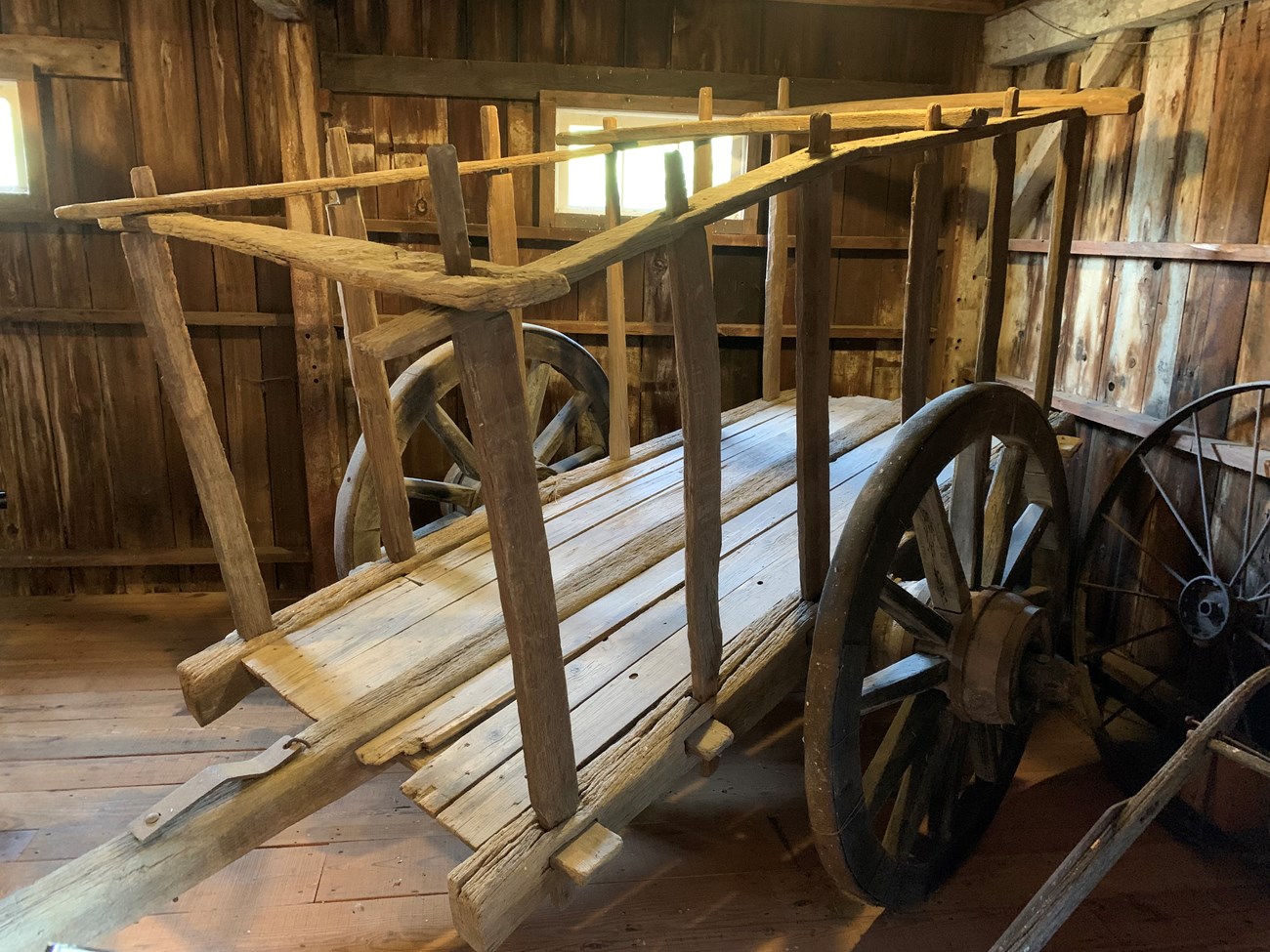Charette in Unconditioned Space Square wagon made of wood with two wheels inside a wooden horse stable.