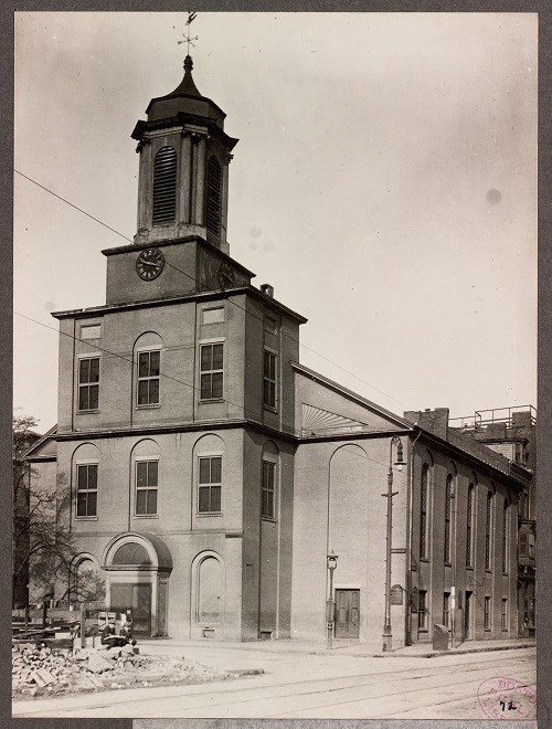 two story church sitting on a corner. Its facade is three stories with a cupola on top.