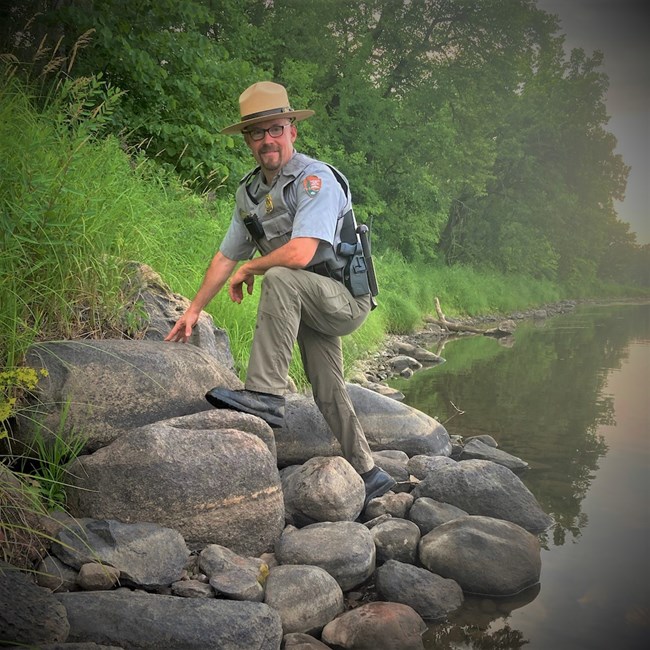 Charlie Lundin on a boulder along a river lined with forest