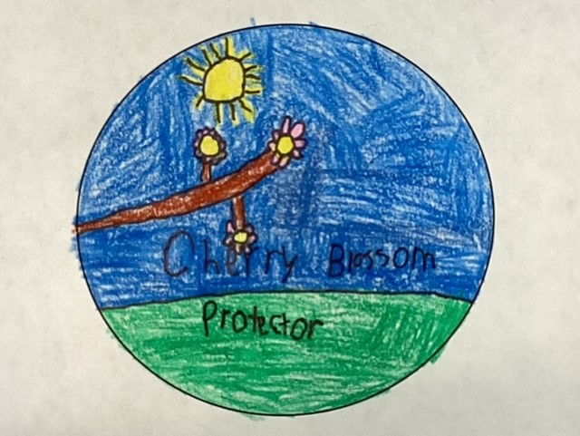 Cherry Blossom Protector Blue Gren Drawing of a branch of a blossoming cherry tree coming into view from the left of a circle against a background of blue above and green below, with a yellow sun above the branch. Handwritten text reads Cherry Blossom Protector