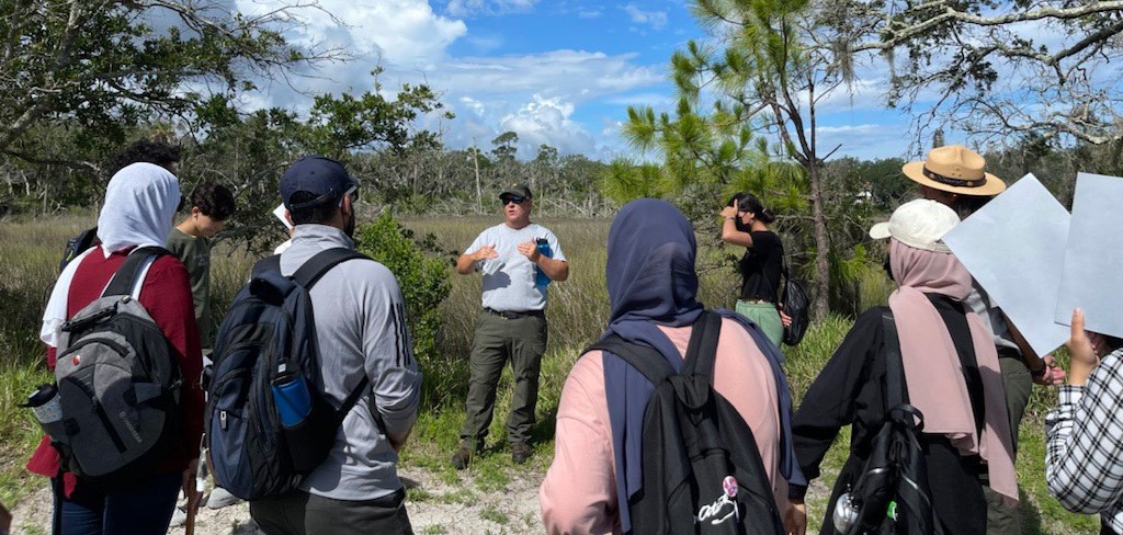 Ches Vervaeke speaks to a group from GlobalJax at Timucuan Ecological and Historic Preserve. Group of people standing around listening to man in a uniform speak