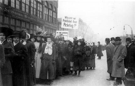 1910 Chicago Garment Workers' Strike Black and white photo of marchers outside on a street. One holds a sign that reads "Why are we prohibited from picketing?"
