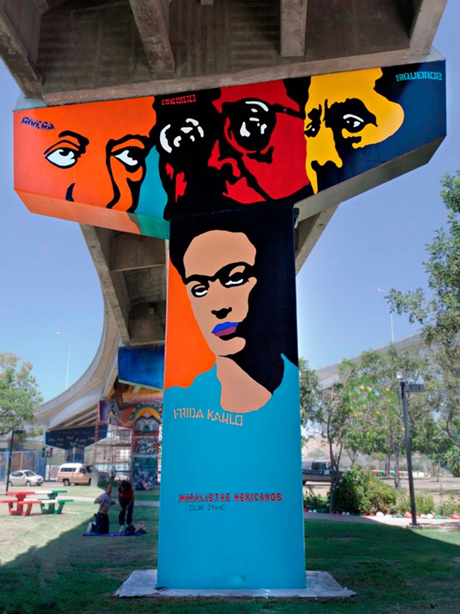 Mural on a T-shaped highway pillar in Chicano Park depicting four famous Mexican muralists: the faces of Diego Rivera, Jose Clemente Orozco, and David Alfaro Siqueiros over the head and shoulders of Frida Kahlo