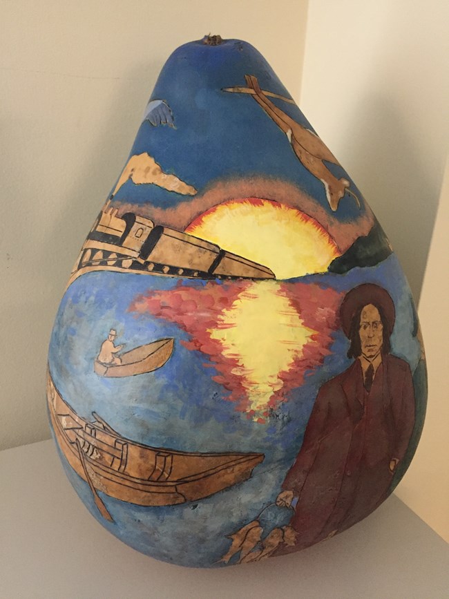 Gourd art depicting two men in front of a river holding fish with a sunset, train, and row boat behind.