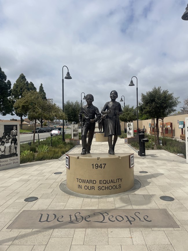Statue of two children on a pedestal with the year 1947 and the phrase "Toward Equality in Our Schools." The sidewalk in front says "We the People"