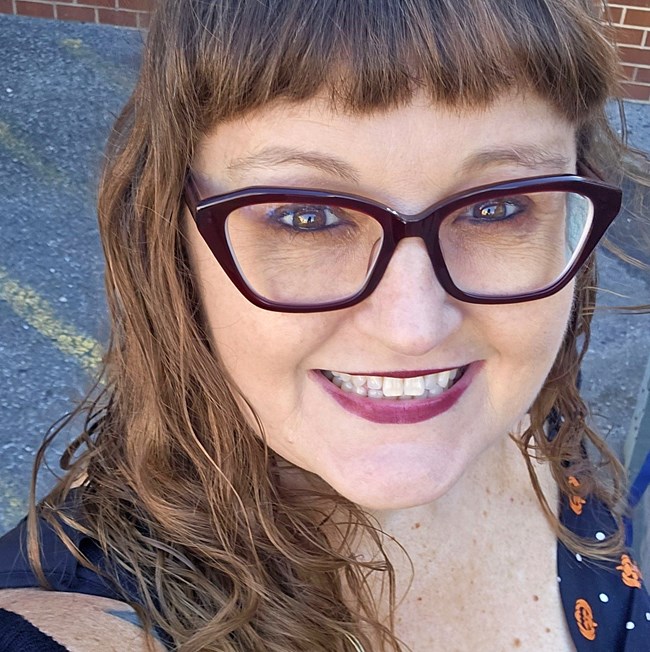 Headshot of a smiling woman with brown eyes and thick-rimmed glasses