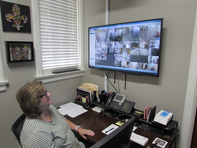 A person is sitting at a desk looking up at a tv monitor that has small images from various parts of the building property.