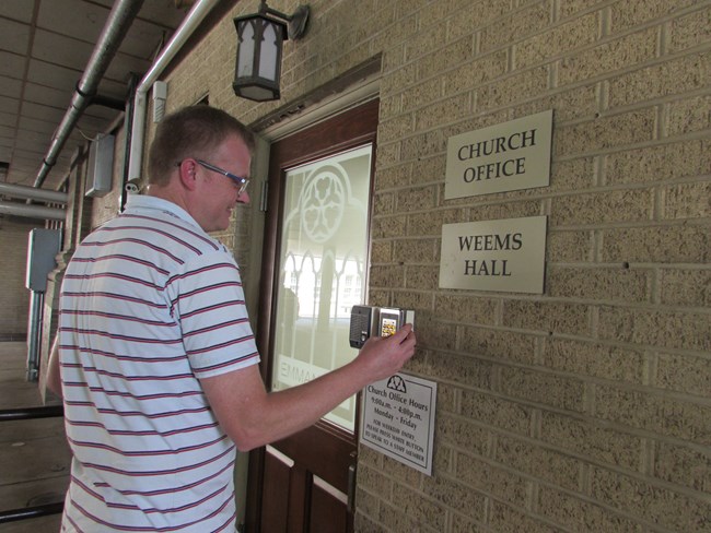 Church staff member uses keypad to access building A man is standing at a door entering a code into a key pad