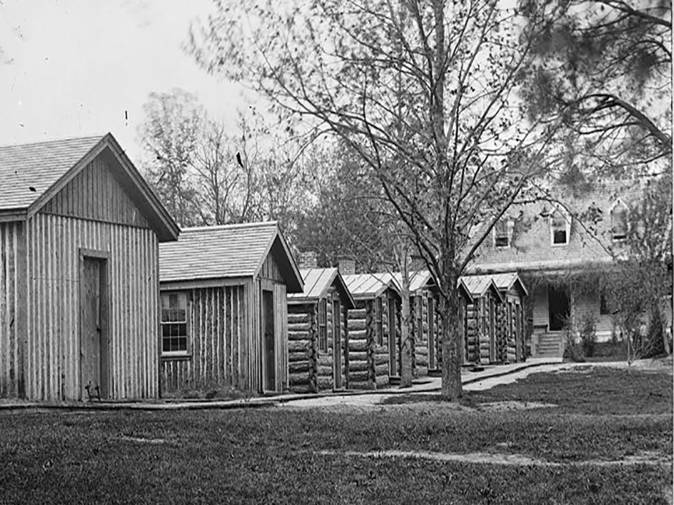 A row of cabins lead to a two story white house.
