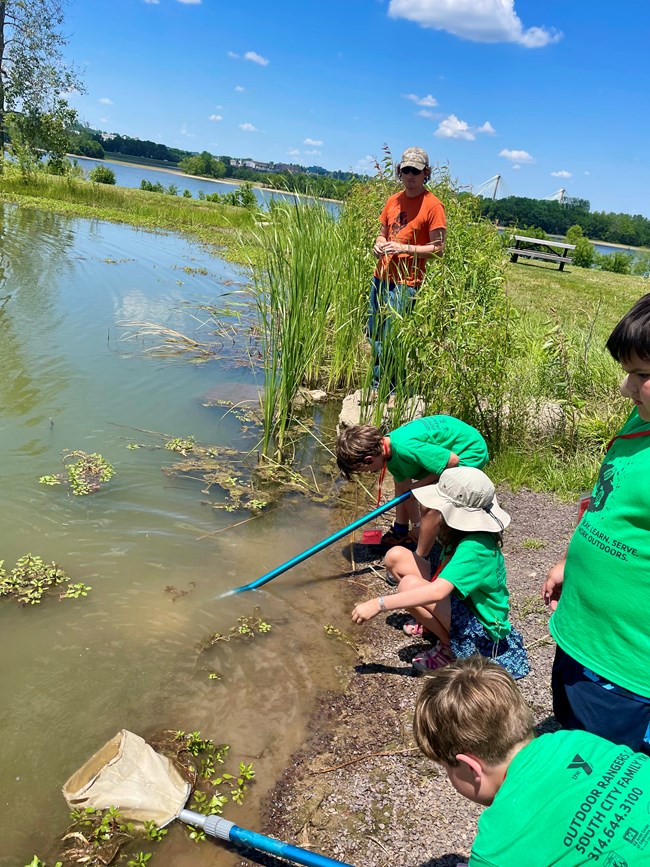 YMCA campers explore waters along the Mississippi River near St. Louis Youth in green shirts use long poles in water from a river
