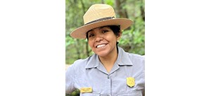 Woman outdoors in a National Park Service hat and uniform, smiling.
