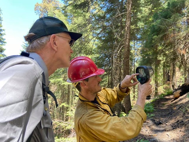 A park ranger and a firefighter view the screen of an infrared camera pointed toward a burned area..