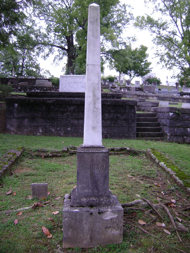 A white obelisk grave marker in a cemetery.