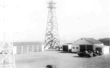 a radio tower sits behind two simple buildings