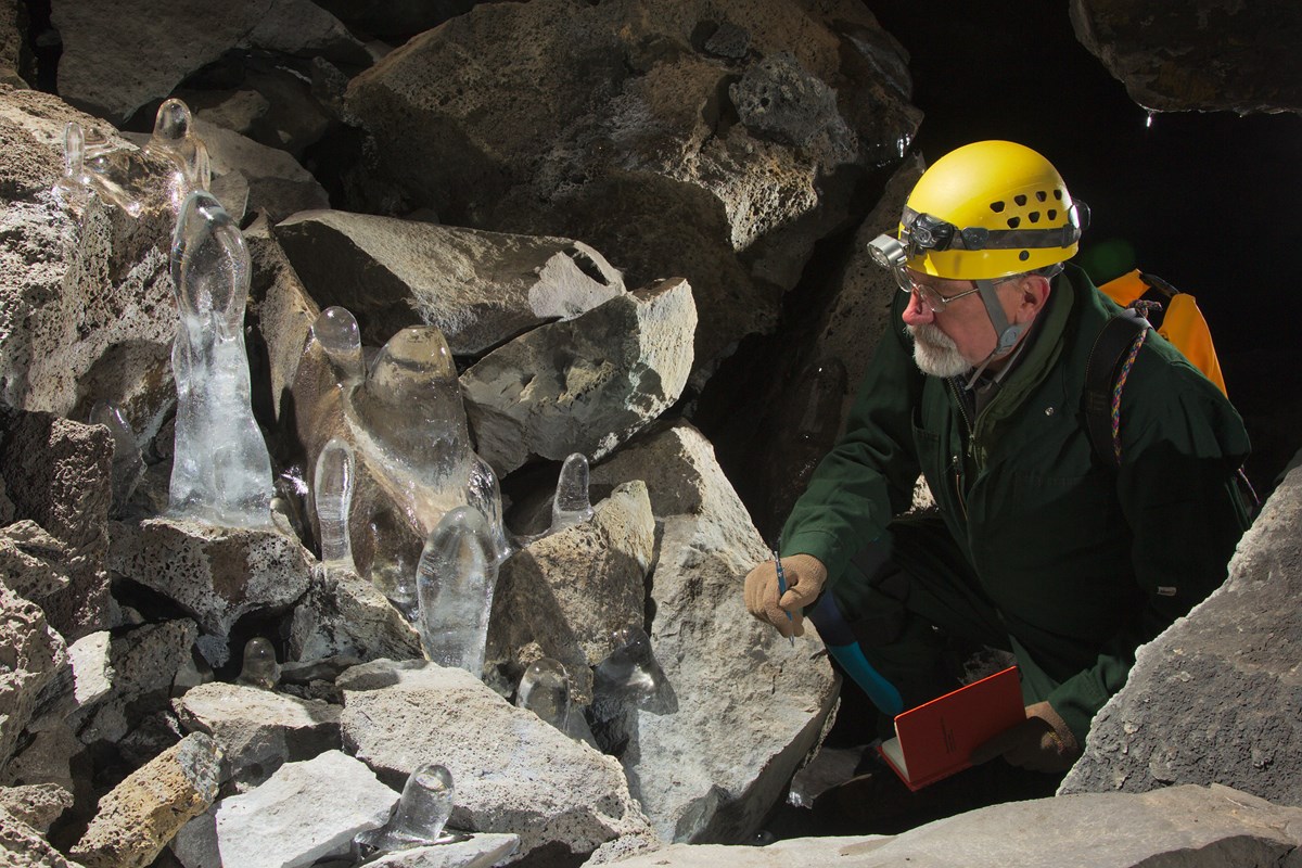 Researcher holding a notebook while crouched in a lava tube looking at ice stalagmites