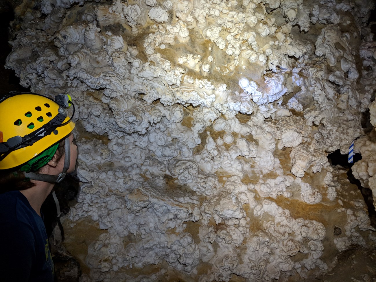 a person wearing a climbing helmet examines crystals on a cave wall
