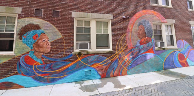 Brick wall with colorful art depicting two African American women.