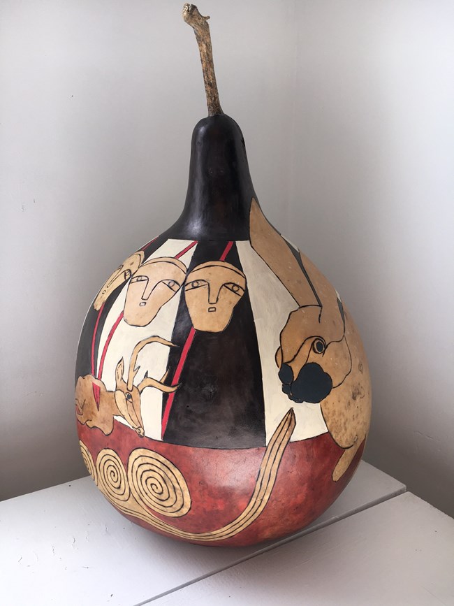 Gourd art depicting a hare, three female faces, and spears piercing a large deer.