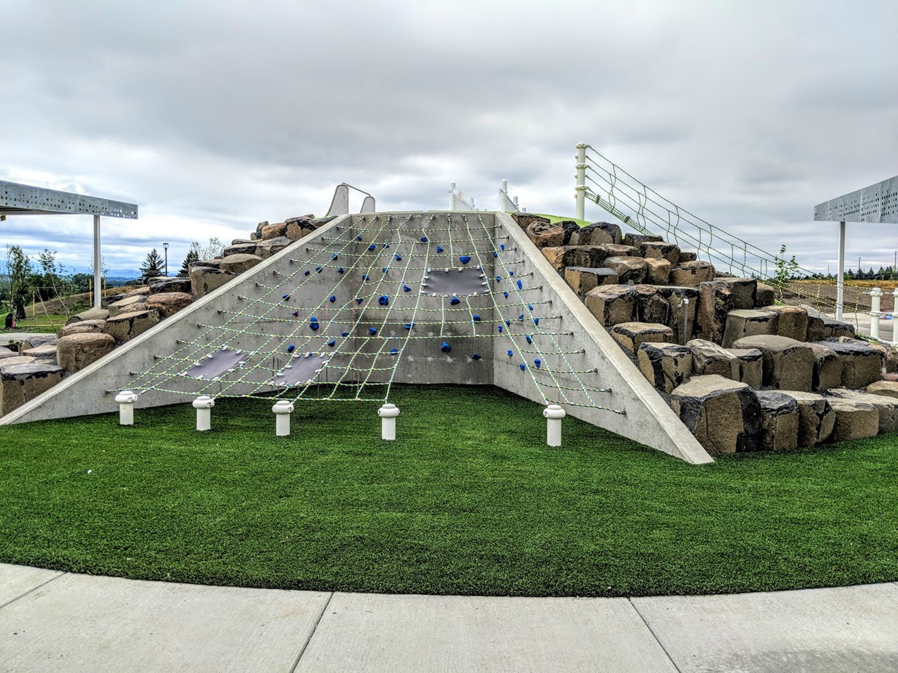 Playground climbing equipment that includes a bouldering area, rock wall, and net