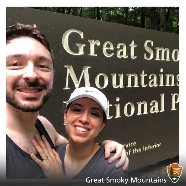Two people taking a selfie in front of a park entrance sign
