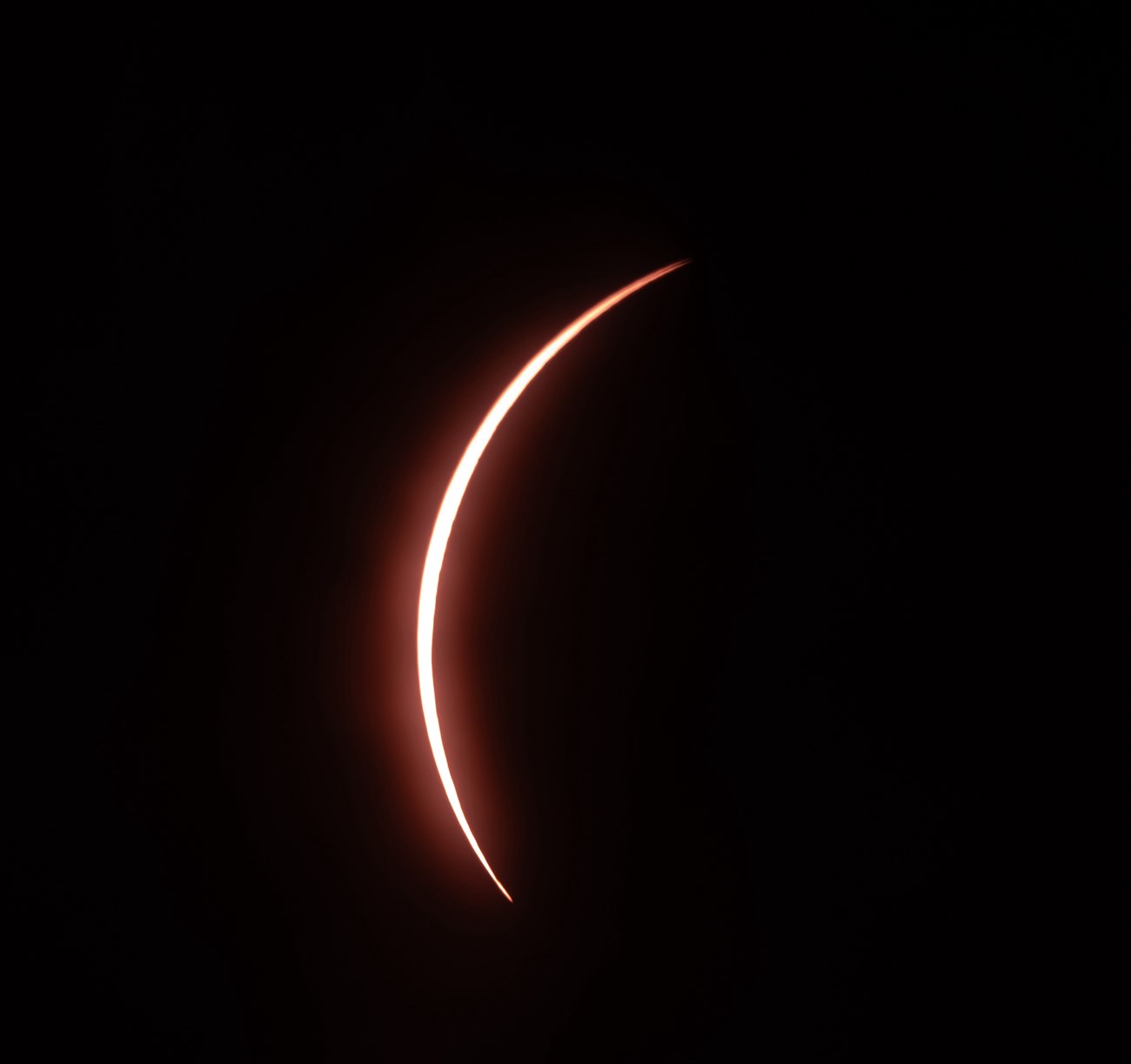 A very thin, bright red sliver of  light pops behind a dark brown-black sphere.