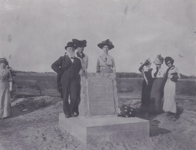 A man and a group of women stand at a monument