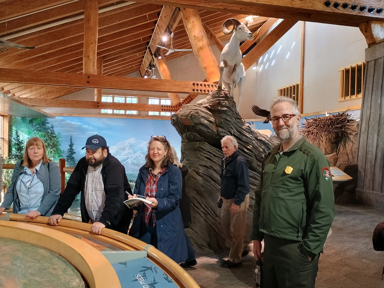 Discussing missing place names Group of people in a visitor center beneath a replica of a dall sheep, looking at an exhibit featuring a 3D map of Denali.