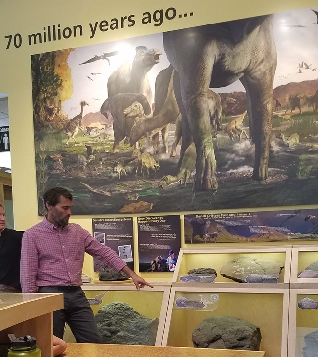 man pointing toward a visitor center display featuring dinosaurs