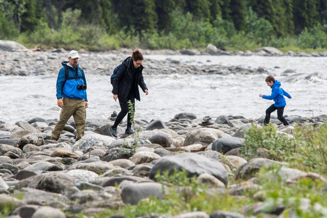 two adult and a child walk on rocks next to a river