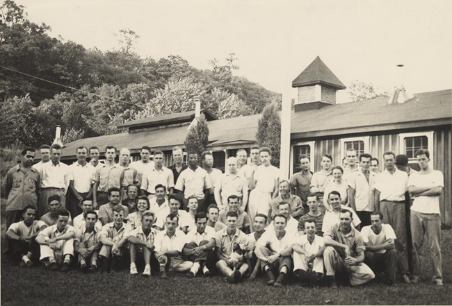 A group of people pose for a group photo in front of a building with trees in the background