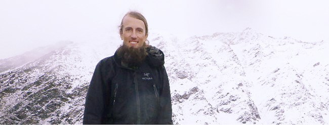 Davyd Halyn Betchkal at Eekayruk Mountain, Gates of the Arctic National Park and Preserve A bearded man dressed in black stands in front of a misty, snow-covered mountain.