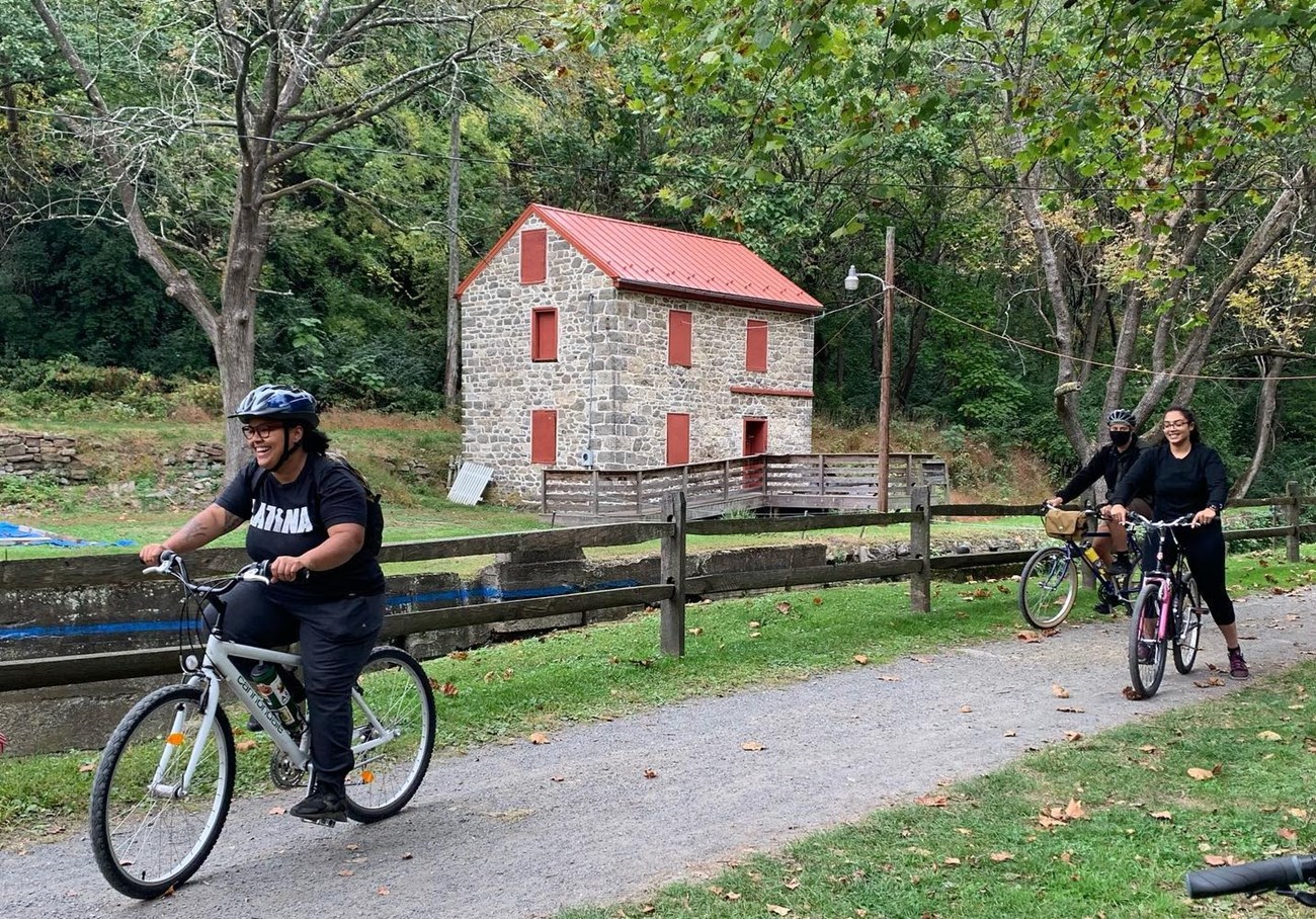 D&L Three bicyclists on bike trail with old stone building with red trim in background