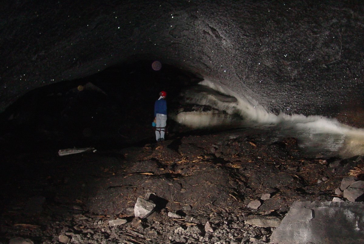 a person standing in a dark cave where ice formations occur along the base of the cave walls